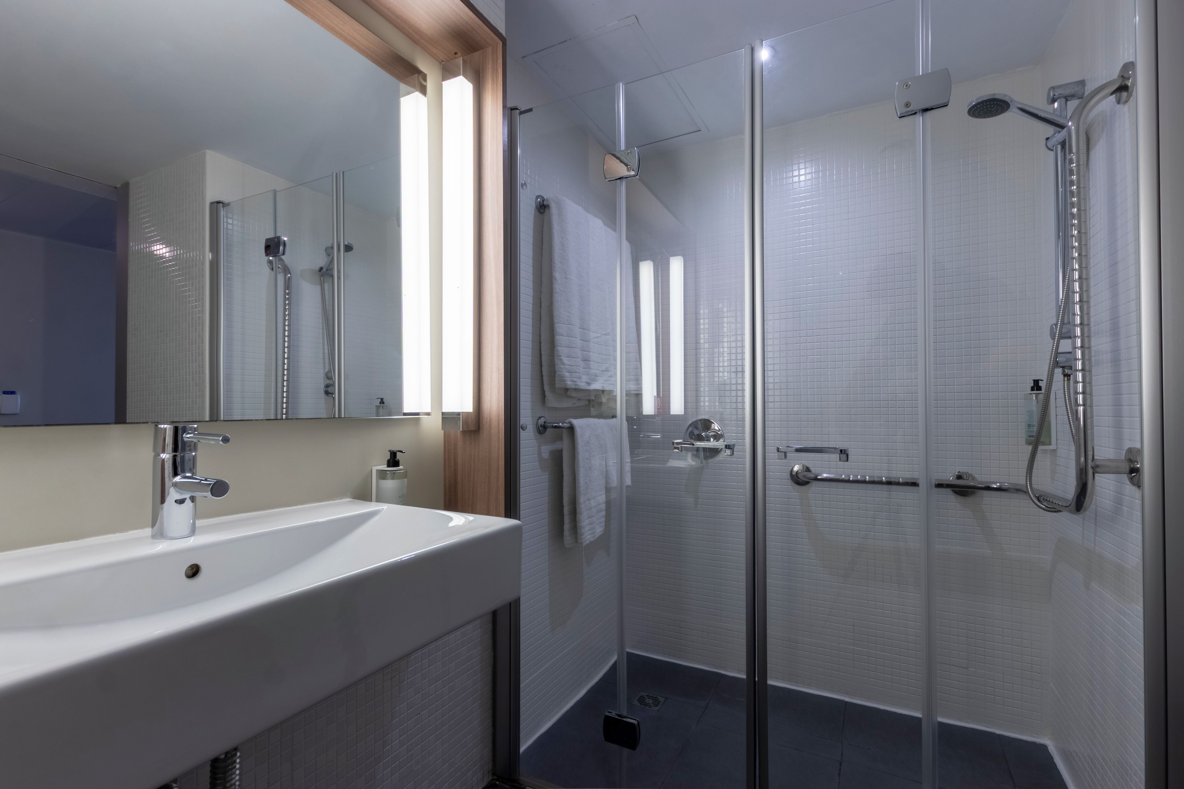 A modern bathroom with a large white sink, a glass-enclosed shower, and a mirror with a wooden frame.