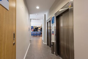 A hallway with a wooden door, a trash bin, and an elevator. - Travelodge Malaga Aeropuerto (Málaga)