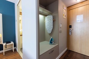A hotel room with a wooden door, a white wall with a hexagonal mirror, a small table with a phone, and a blue iron. - Travelodge Malaga Aeropuerto (Málaga)
