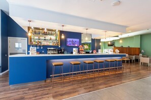 A bar area with a blue counter, multiple stools, and a variety of bottles and glasses. - Travelodge Malaga Aeropuerto (Málaga)