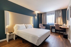 A hotel room with a bed, bedside table, desk, chair, and a small kitchenette. - Travelodge Malaga Aeropuerto (Málaga)