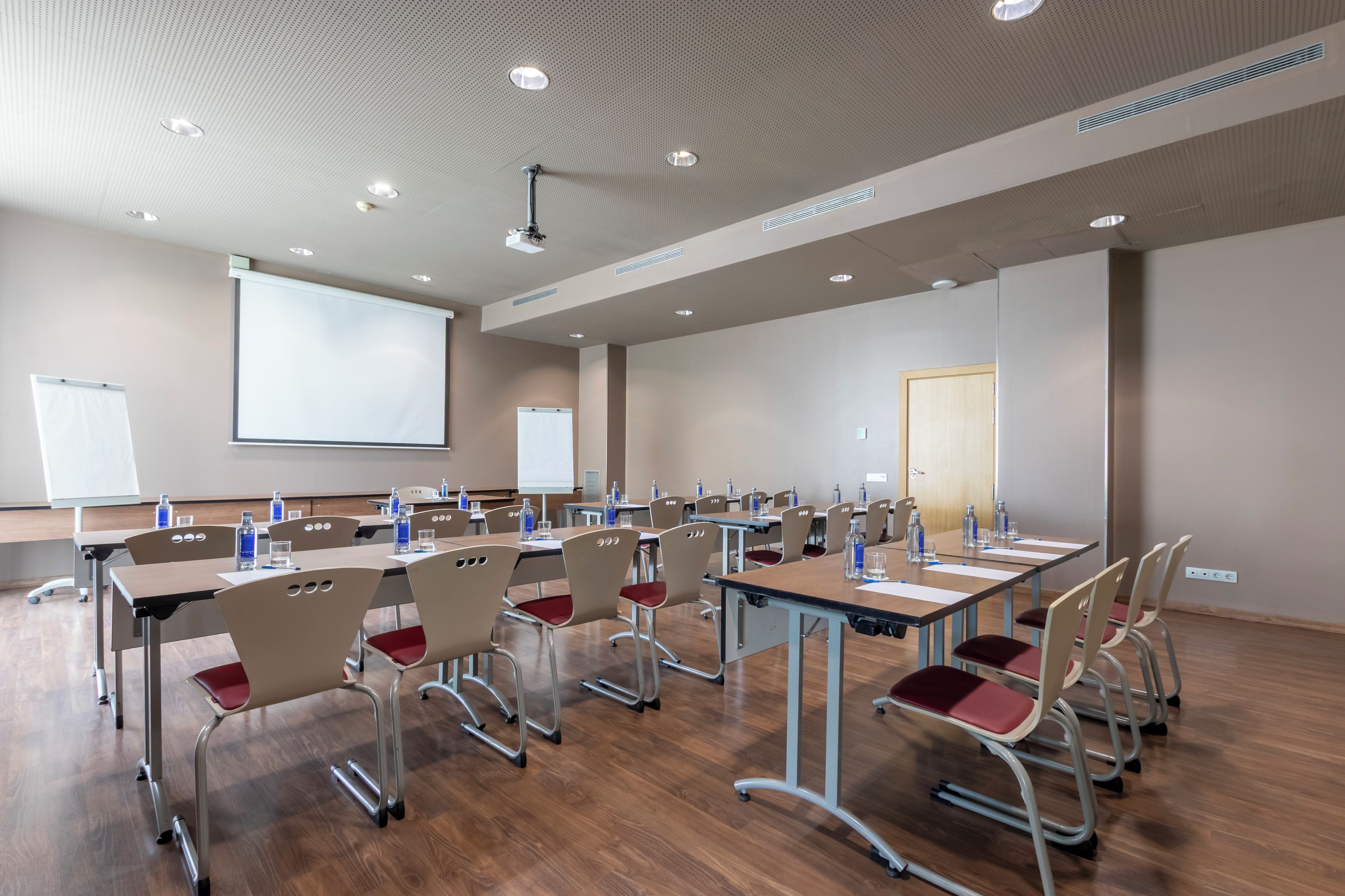 A conference room with multiple tables and chairs, a projector screen, and a whiteboard.