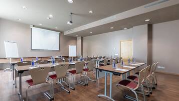 Una sala de conferencias con varias mesas y sillas, una pantalla de proyector y una pizarra.
