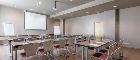 Une salle de conférence équipée de plusieurs tables et chaises, d’un écran de projection et d’un tableau blanc.