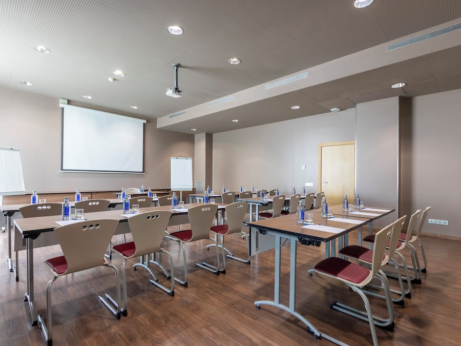 Una sala de conferencias con varias mesas y sillas, una pantalla de proyector y una pizarra.