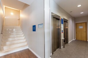 A clean, modern hallway with a staircase, two elevators, and a wooden door. - Travelodge Malaga Aeropuerto (Málaga)