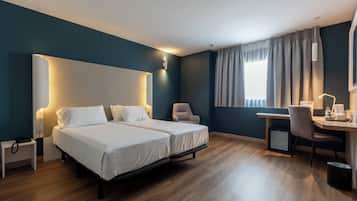 Habitación de hotel con dos camas, un escritorio, una silla y una pequeña cocina.