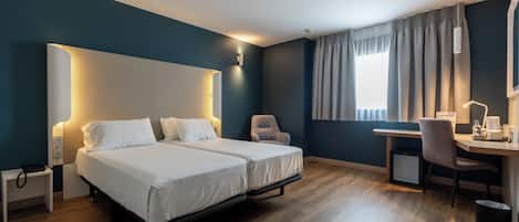 Habitación de hotel con dos camas, un escritorio, una silla y una pequeña cocina.