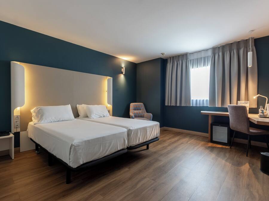 Habitación de hotel con dos camas, un escritorio, una silla y una pequeña cocina.
