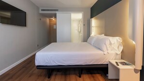 Une chambre d’hôtel moderne équipée d’un lit, d’une table de chevet et d’un téléviseur à écran plat fixé au mur.