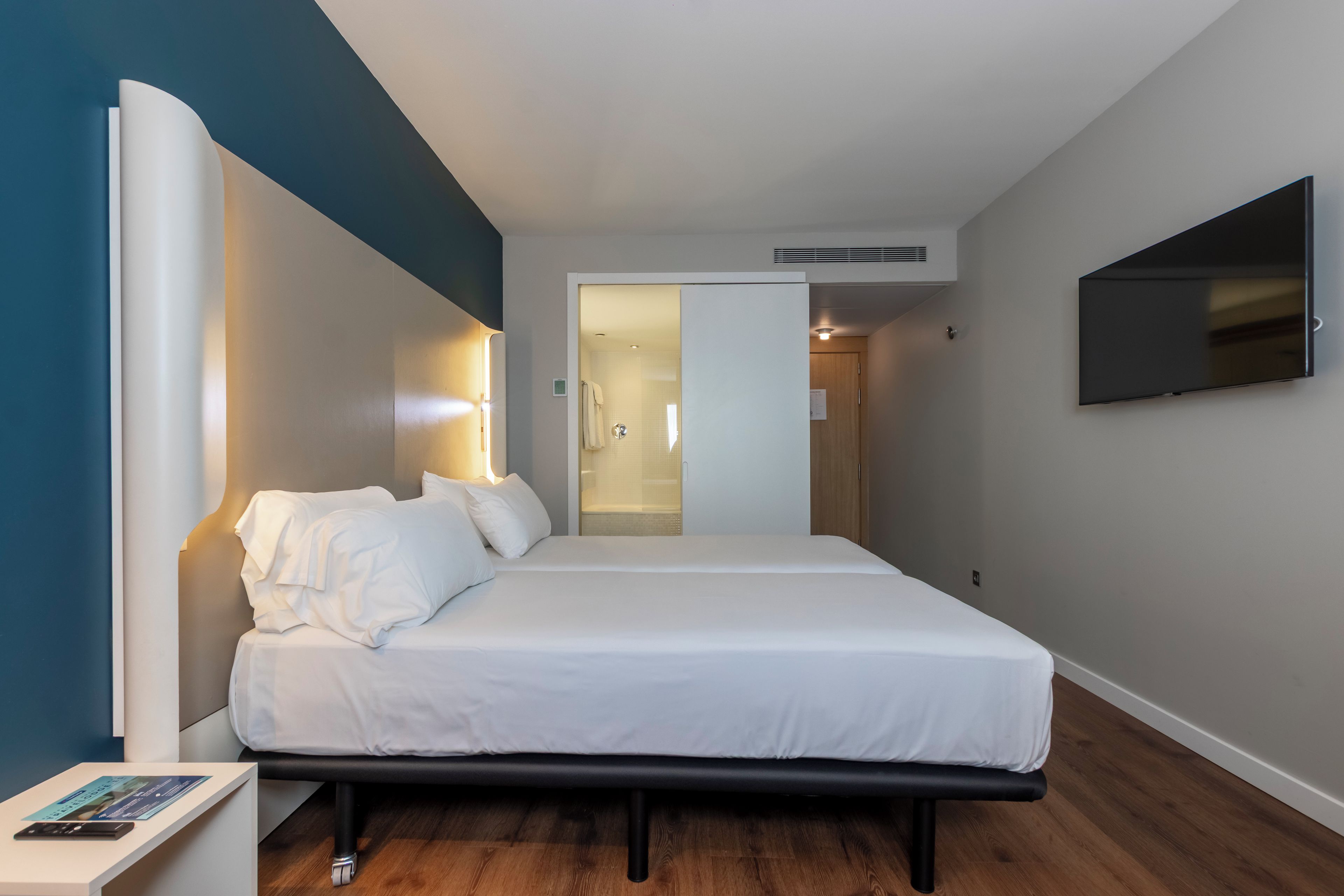 Quarto de hotel moderno com cama, mesa de cabeceira e TV de tela plana na parede.
