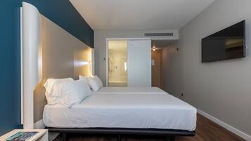 Quarto de hotel moderno com cama, mesa de cabeceira e TV de tela plana na parede.