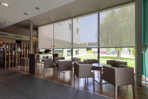 A modern indoor seating area with large windows, a reception desk, and a view of the outside. - Travelodge Malaga Aeropuerto (Málaga)