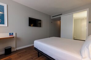 A hotel room with a bed, a mounted TV, a small shelf, and a trash bin. - Travelodge Malaga Aeropuerto (Málaga)