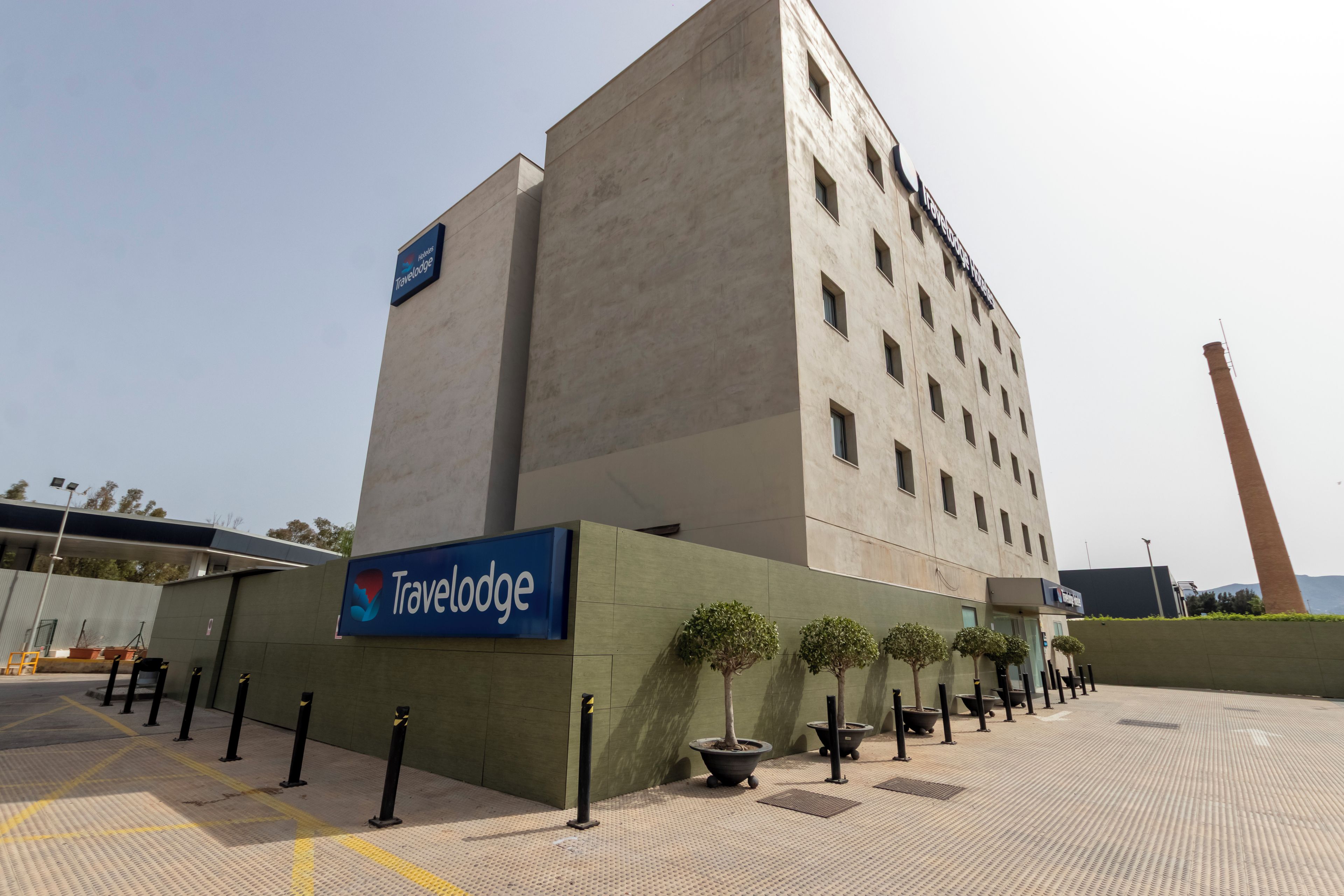 Un hotel Travelodge de diseño moderno, con un letrero llamativo, un amplio estacionamiento y una chimenea alta al fondo.