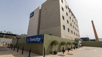 Un hotel Travelodge de diseño moderno, con un letrero llamativo, un amplio estacionamiento y una chimenea alta al fondo.