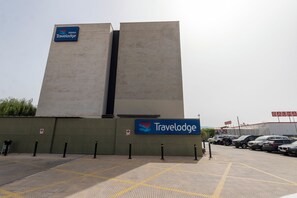 A Travelodge hotel with a modern design, featuring a prominent sign and a parking area with tactile paving for the visually impaired. - Travelodge Malaga Aeropuerto (Málaga)