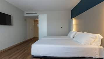 A modern hotel room with a large bed, a flat-screen TV mounted on the wall, and a wooden floor.
