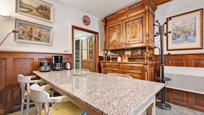 Cozinha com bancada de granito, armários de madeira e área de jantar com uma cadeira branca.
