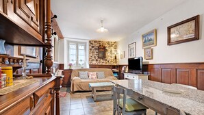 Uma cozinha com armários de madeira, parede de pedra, sala de jantar com mesa e cadeiras, e uma televisão.