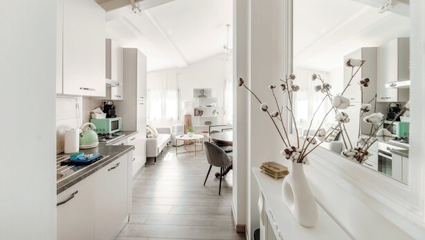 A modern kitchen with white cabinets, a green microwave, and a dining area with a round table and chairs. - Boheme Loft (Como)