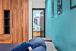 Ein Schlafzimmer mit Holzschrank, einem Bett mit blauer Decke, einem Badezimmer mit Spiegel und Waschbecken sowie Wänden in Türkis.