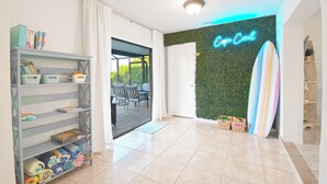 A room with a surfboard, a neon sign, and a shelf with folded towels.