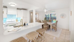 A modern kitchen with white cabinetry, a large island with bar stools, and a dining area with wicker chairs.