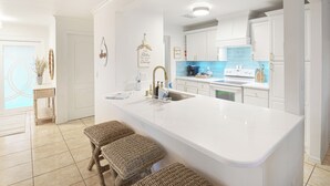 A modern kitchen with white cabinetry, a large island with stools, and a blue backsplash.
