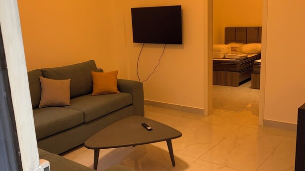 A living room with a sofa, a coffee table, and a flat-screen TV mounted on the wall.
