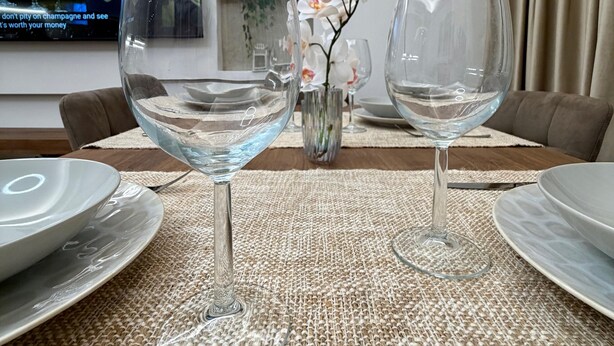 A dining table with two empty wine glasses, a vase with flowers, and a television in the background. - House Gordiani Comfort Stay (Roma)