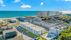 A coastal hotel area with multiple buildings, a swimming pool, and a view of the ocean.