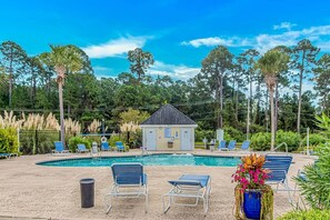 A pool area with lounge chairs, a small building, and surrounding trees.