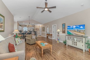 A spacious living area with a ceiling fan, a dining table, and a TV on a stand.