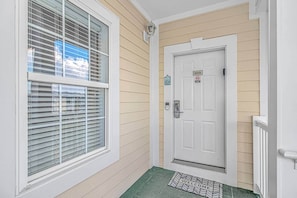 A white door with a number sign, a window with blinds, and a welcome mat.