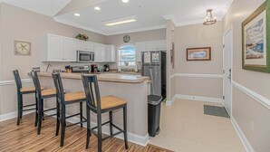 Cocina moderna con armarios blancos, una isla central con taburetes de bar, un refrigerador y un microondas.