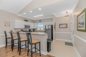 Une cuisine moderne avec des meubles blancs, un îlot central doté de tabourets, un réfrigérateur et un four à micro-ondes.
