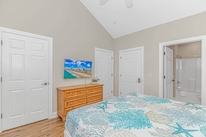 A bedroom with a bed, a dresser, a TV on the wall, and two doors.