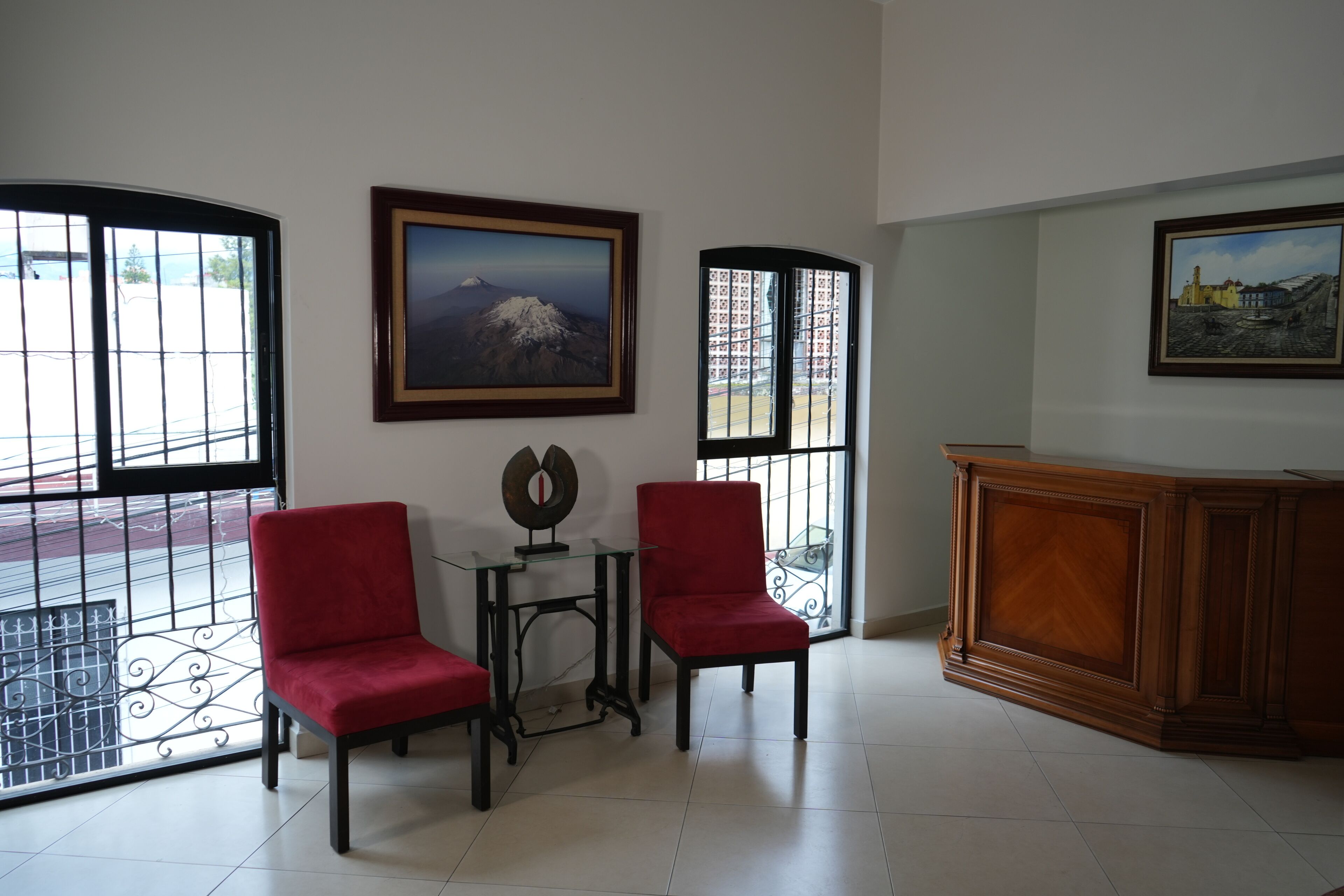 Una habitación con dos sillas rojas, una mesa de vidrio, un armario de madera y dos cuadros en las paredes.