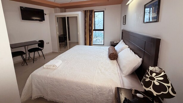 A bedroom with a large bed, a desk, a chair, a TV, and a window with curtains. - Rolovi Xalapa Hotel (Xalapa)