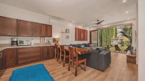 A modern kitchen with wooden cabinets, a dining area with a blue rug, and a living space with a sofa and a TV. - Casa Mercurio (San Pancho)