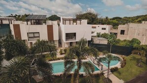 A modern residential area with a swimming pool surrounded by palm trees, solar panels on rooftops, and a clear sky. - Casa Mercurio (San Pancho)