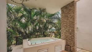 A spa area with a large bathtub, a stone wall, and lush greenery in the background. - Casa Mercurio (San Pancho)