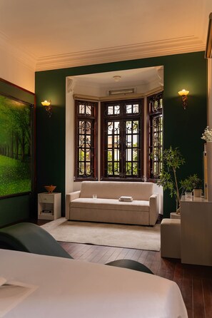 A room with a bed, a sofa, a window with decorative iron bars, a wall-mounted lamp, and a framed painting. - Villa Paradise 6Bedroom (Thu Duc)