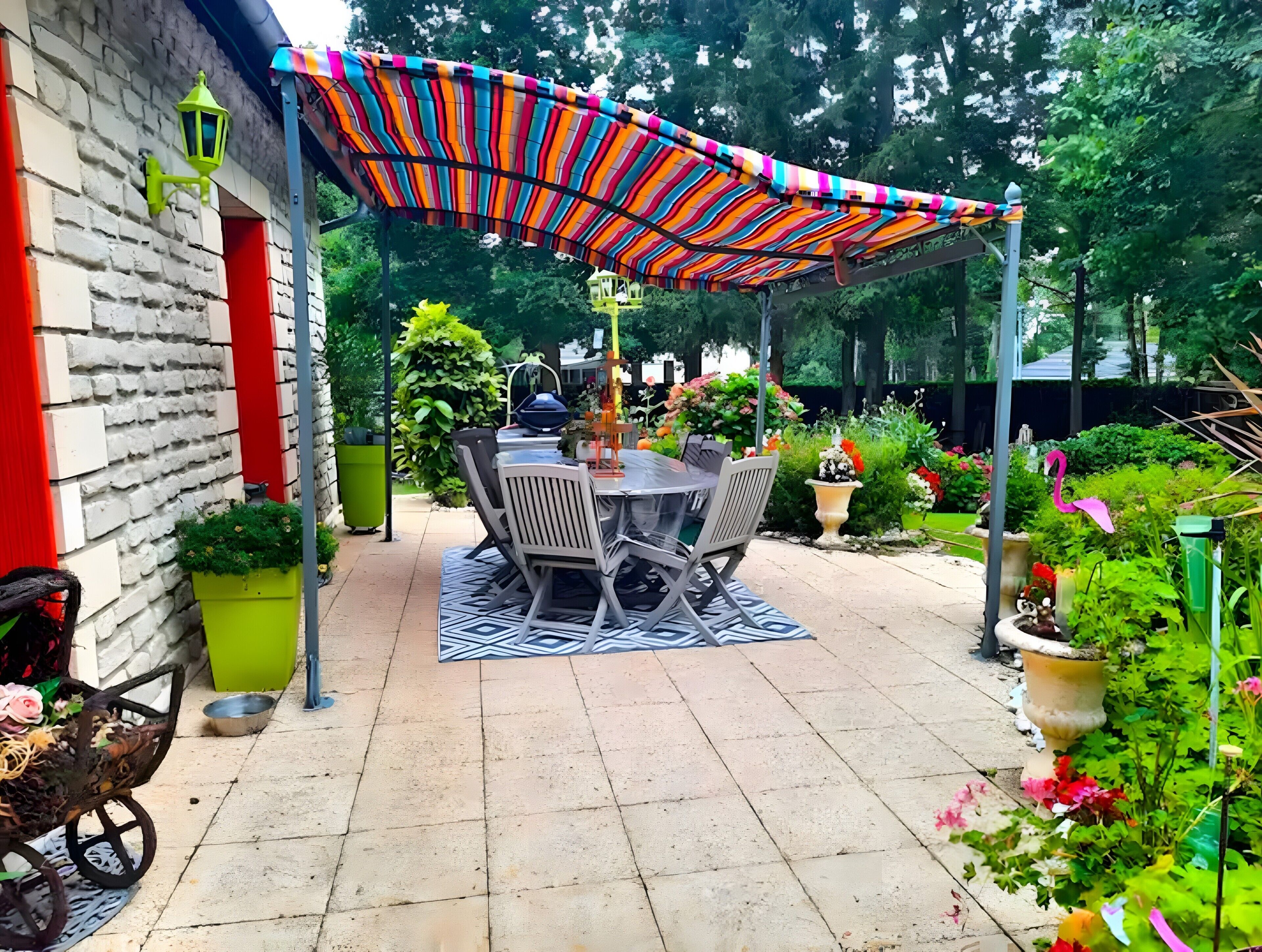 Une terrasse avec une table et des chaises, entourée de plantes en pot et d’un auvent rayé aux couleurs vives.
