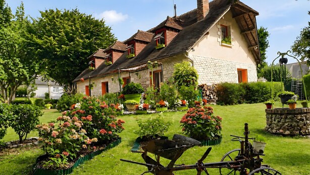 Una casa de piedra tradicional con techo inclinado, rodeada por un jardín bien cuidado con diversas plantas y flores.