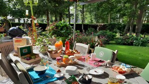 Un área de comedor al aire libre con una mesa dispuesta para el desayuno, rodeada de follaje y árboles.