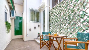A small patio area with a wooden table and chairs, a green door, and a wall with a lattice design. - Cool Style Private Apartments (Dafni-Ymittos)