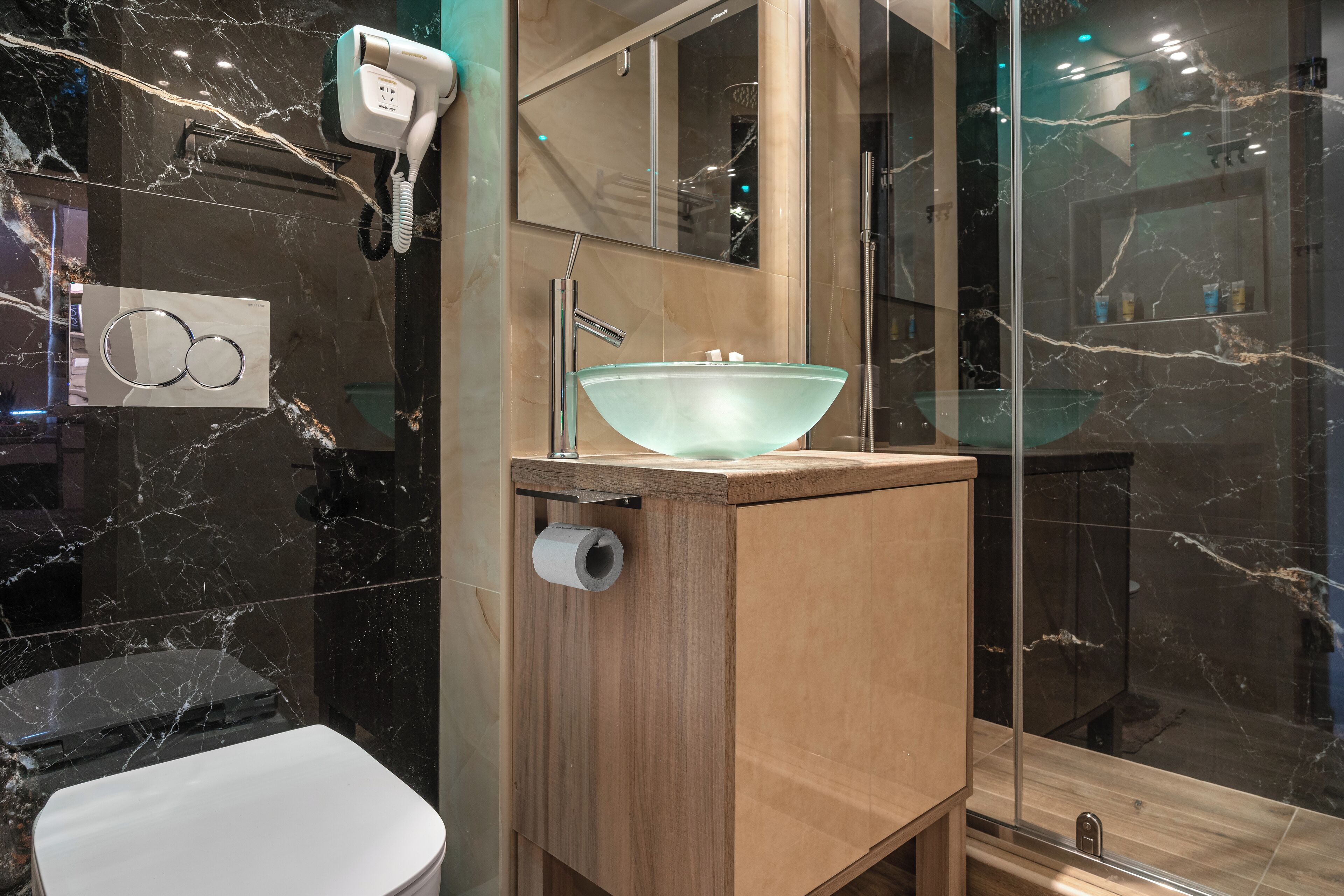 A modern bathroom with a glass sink, a hairdryer, and a toilet.