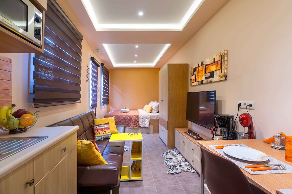 Un espace de vie compact comprenant un coin cuisine, un espace repas et un lit.